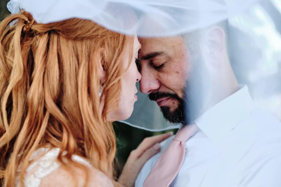 a bridal couple with eyes closed and heads together standing under veil