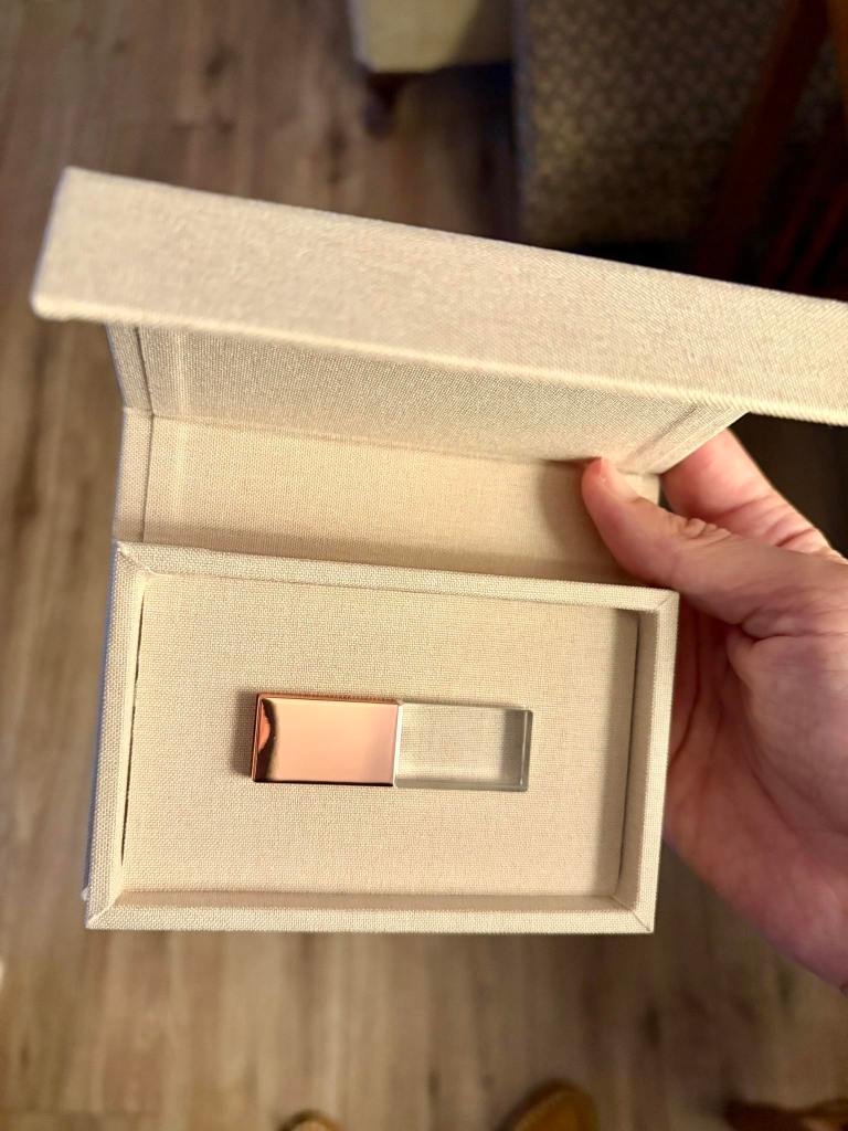 a photograph of someone holding a cream linen keepsake USB box, with a crystal and rose gold colored USB drive in the box