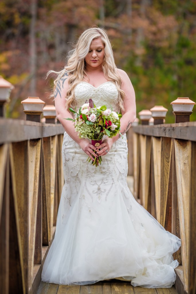 a bride standing on the bridge of a dock, photographed from a lower than railing vantage point. Bride is looking down at her bouquet